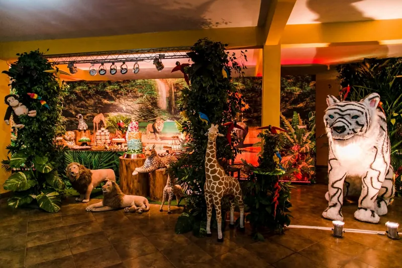 Cenário de festa infantil de safári, com girafa, leões e um tigre branco de pelúcia entre folhagens
